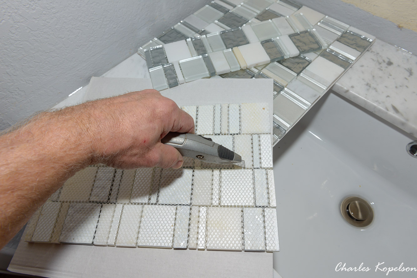 My backsplash is going to be 4" with the tile vertical so I'm cutting a 12" glass mosaic in thirds. I'm cutting on top of the corregated mat that the sheets of mosaic came with. You don't want to scratch your brand new top with a razor knife.